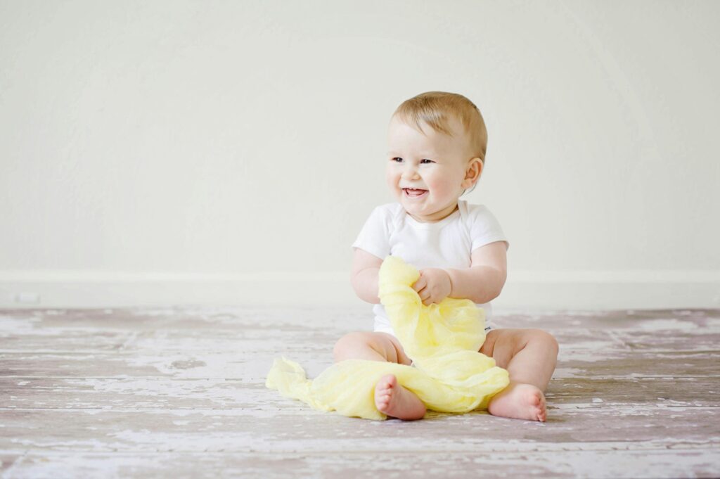 Adorable baby laughing while sitting on the floor with a yellow blanket indoors, showcasing happiness and innocence.